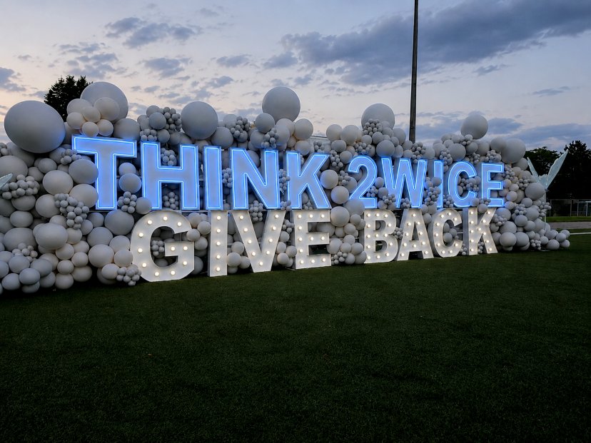 Balloon wall with glowing THINK 2WICE and GIVE BACK letters at dusk