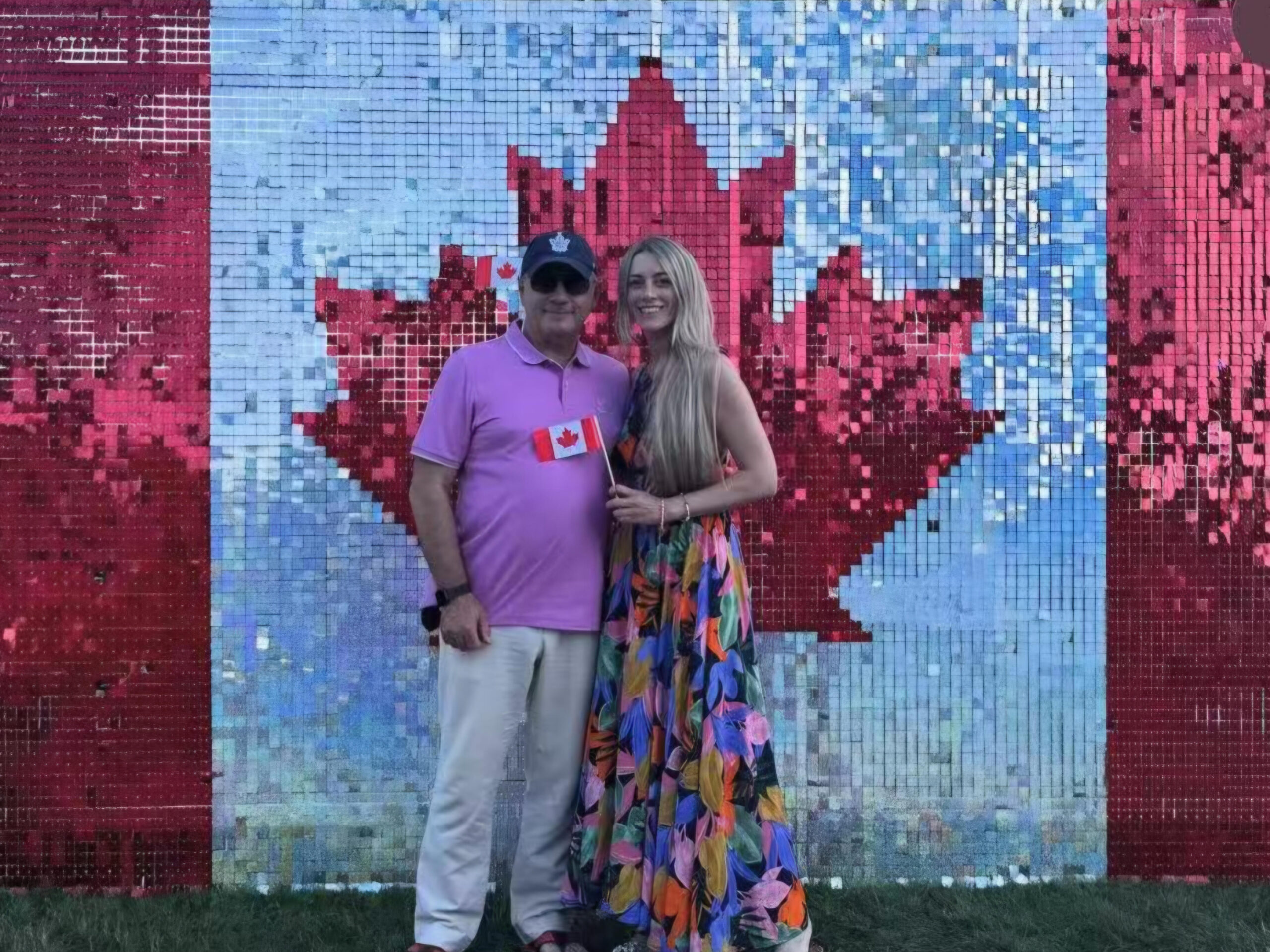 Couple holding a Canadian flag before a sequin maple leaf wall