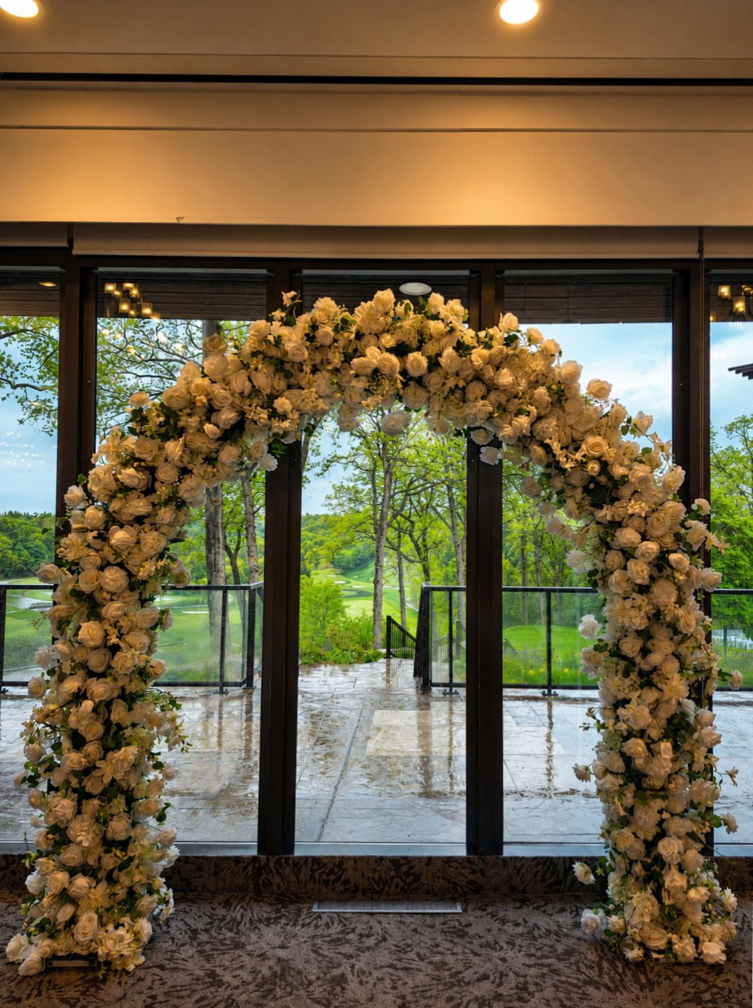 White rose floral arch before tall windows overlooking a garden terrace