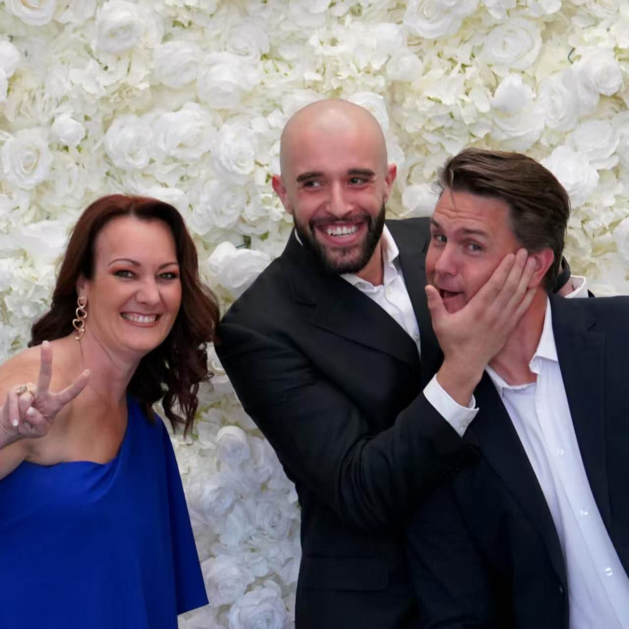 Three guests posing playfully before a white rose wall