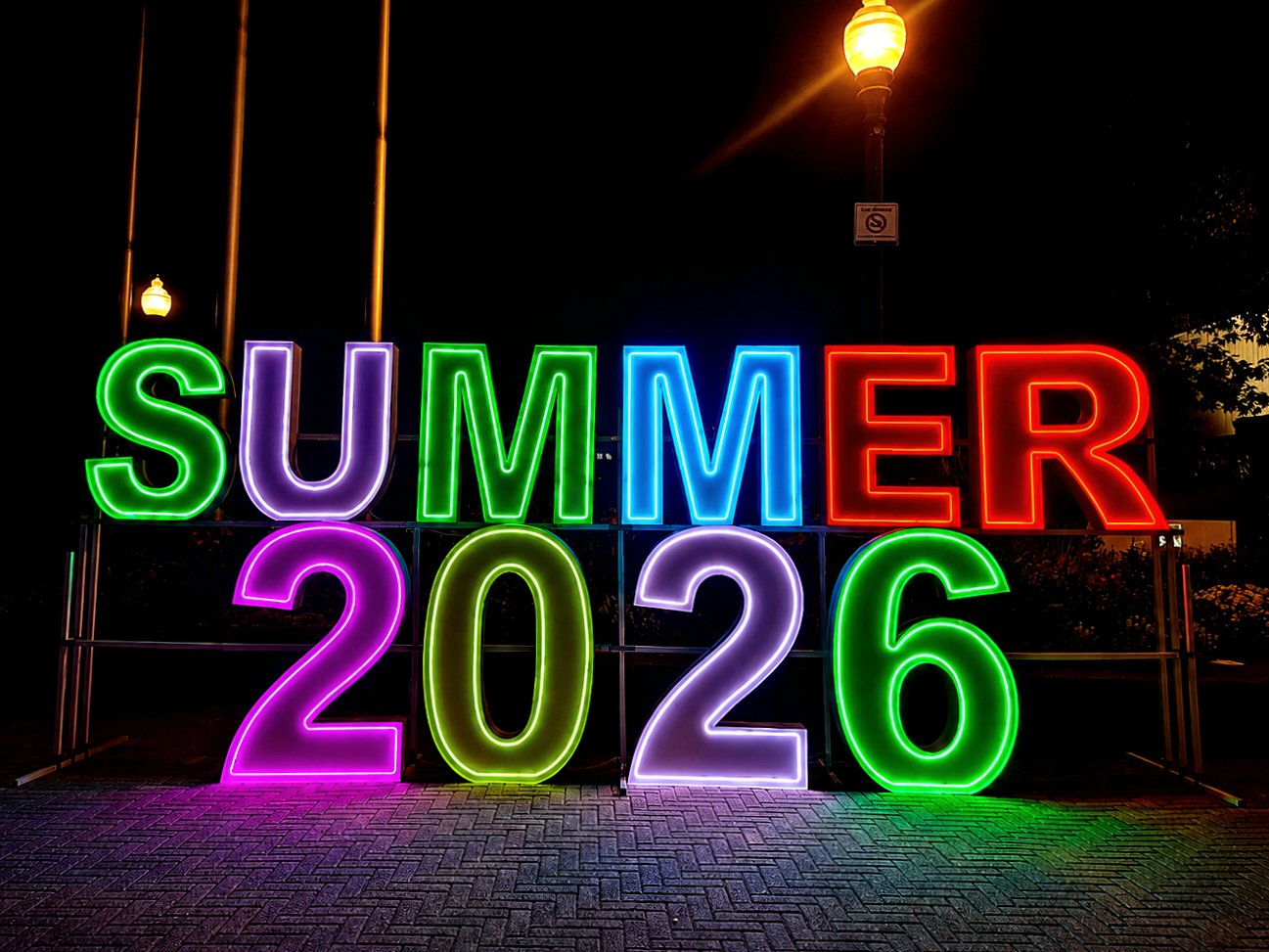 Colorful neon letters spelling SUMMER 2026 glowing at night