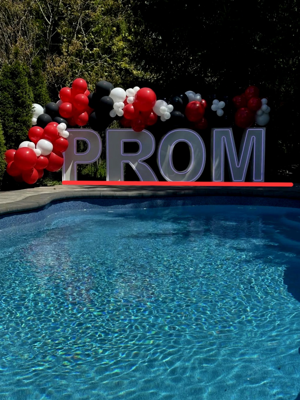 Illuminated PROM letters with red, black and white balloons by a pool