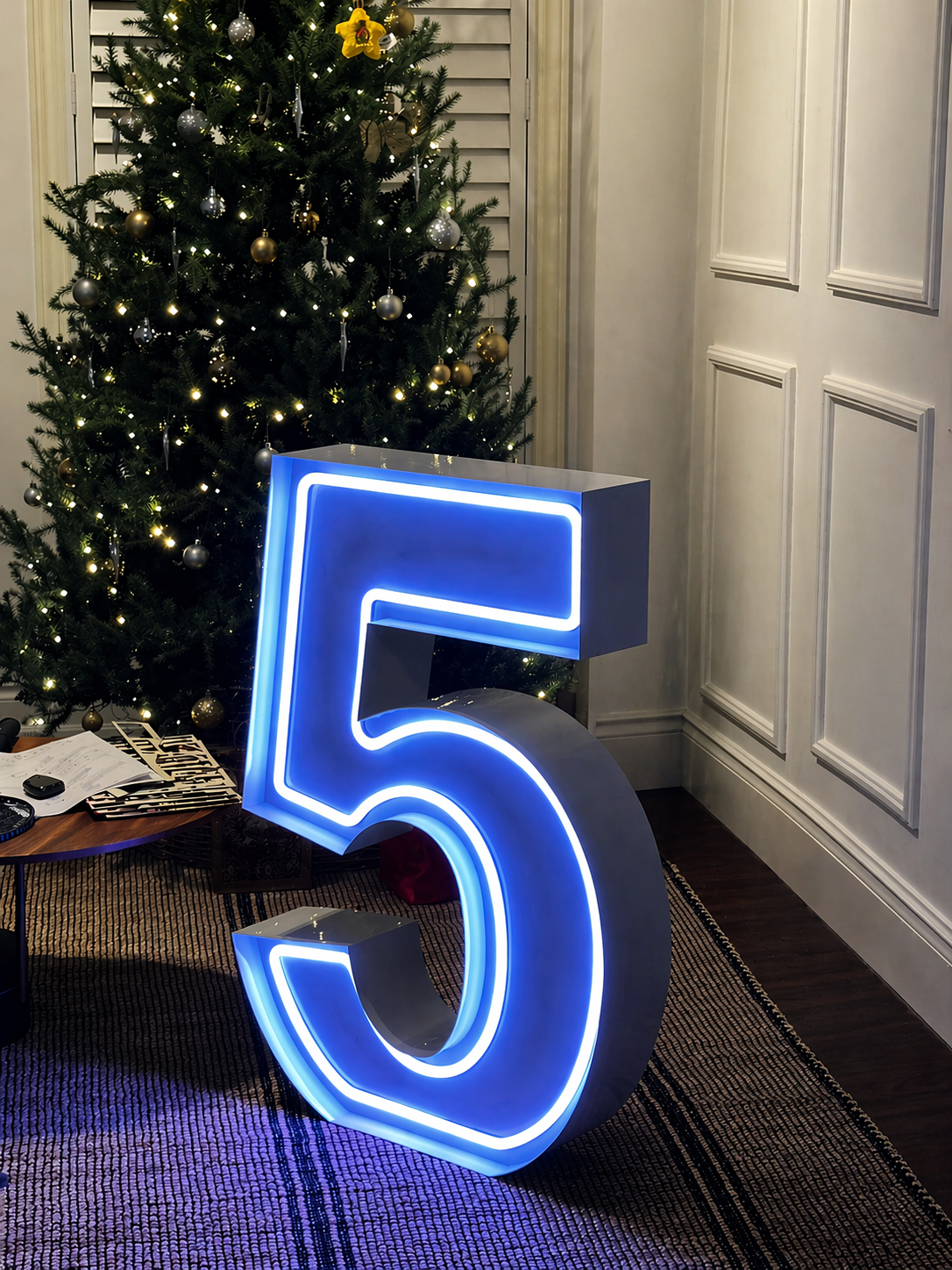 Large blue neon number 5 beside a decorated Christmas tree