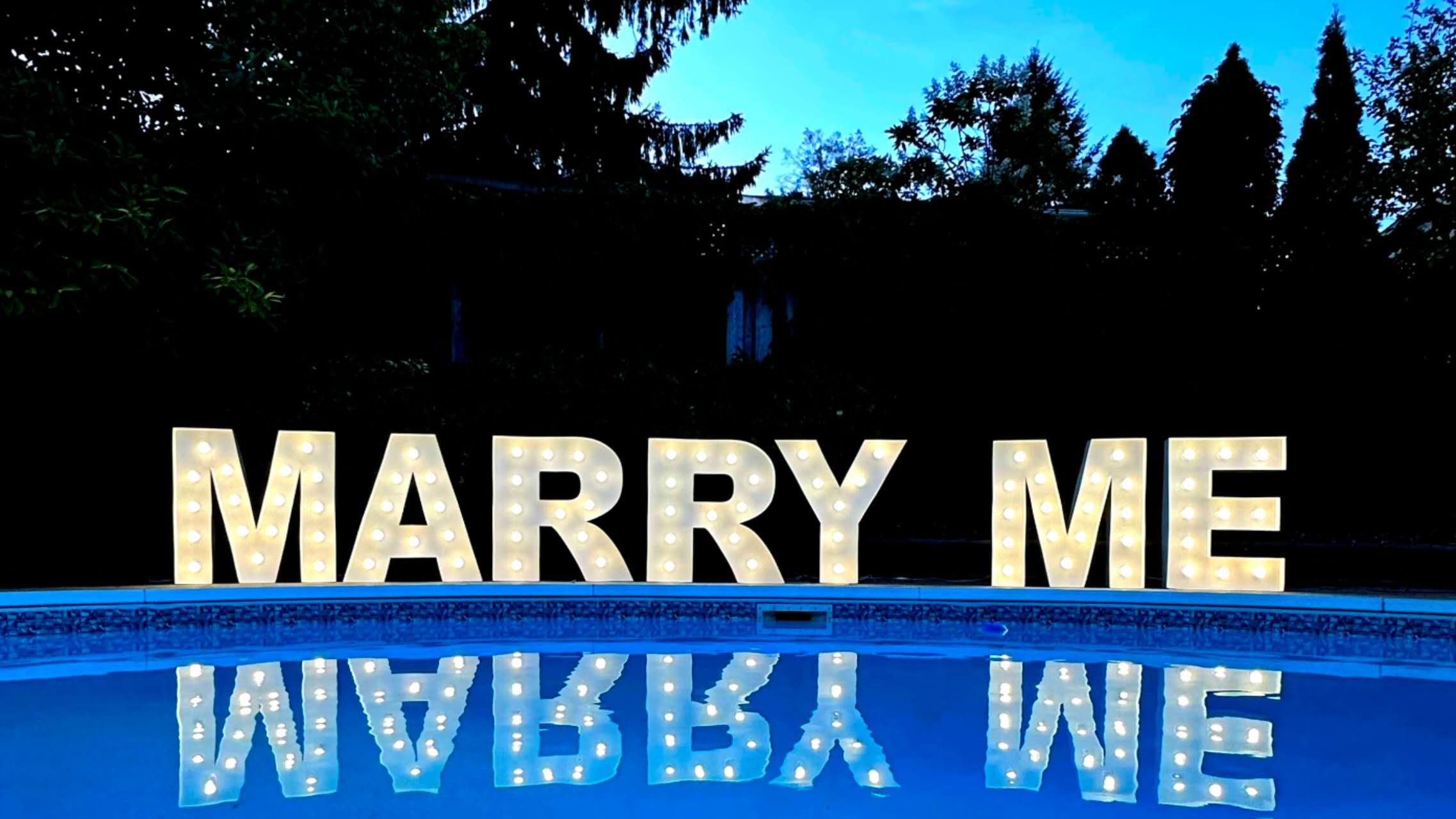 LED MARRY ME bulb letters by a pool at dusk with reflection