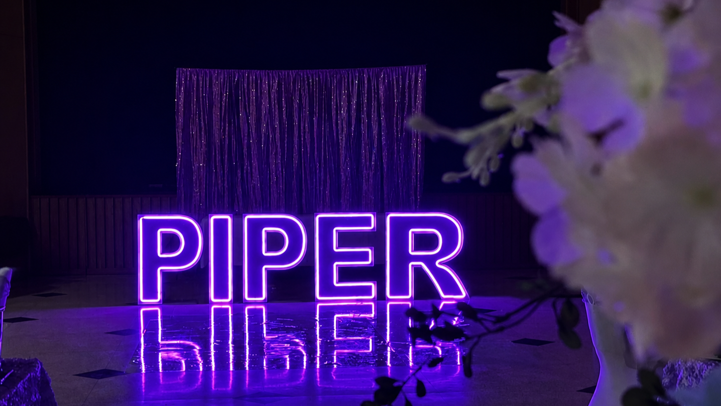 Purple neon letters spelling PIPER reflected on a glossy floor
