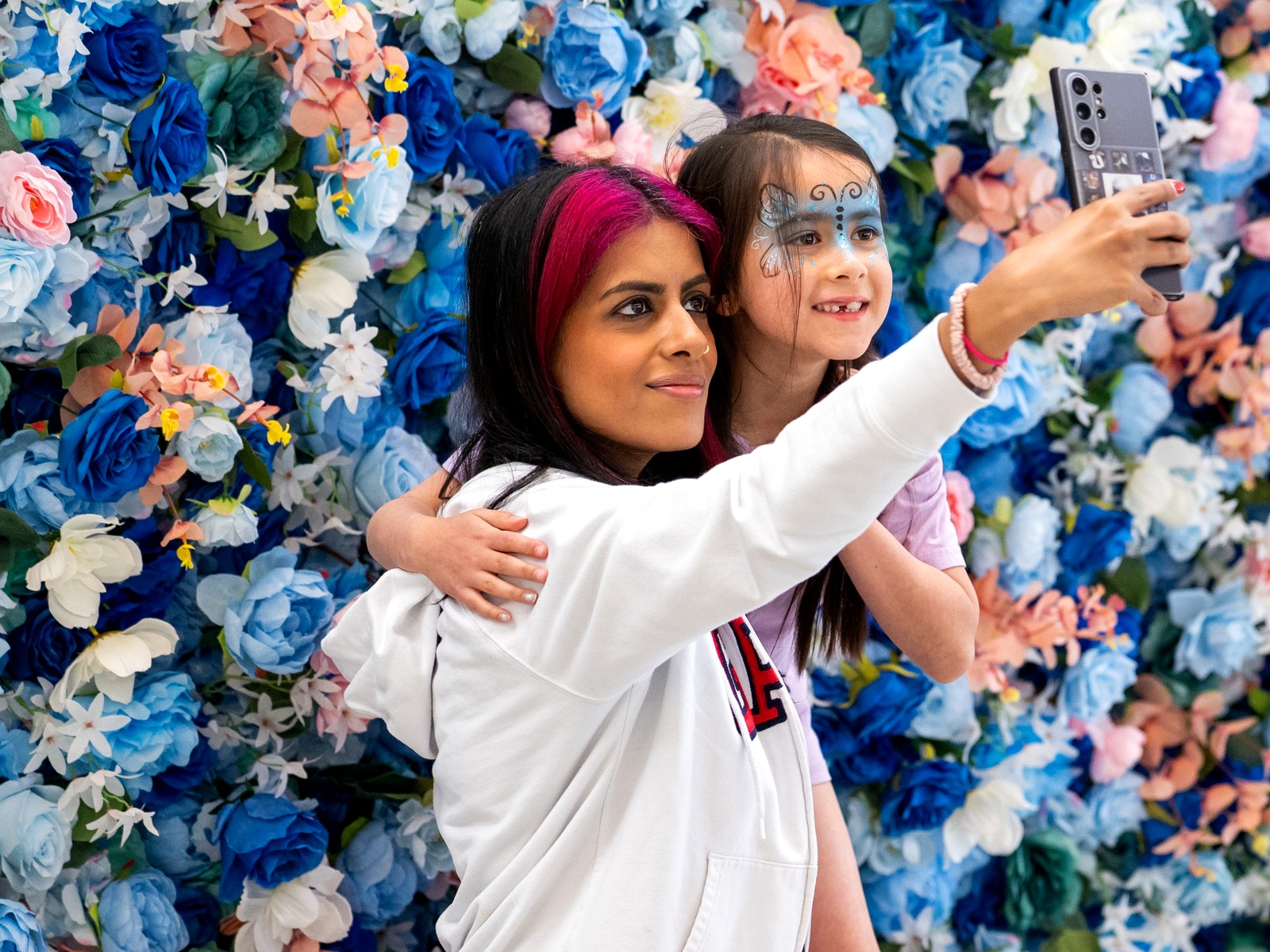 Mother and child taking a selfie at the blue and pink flower wall