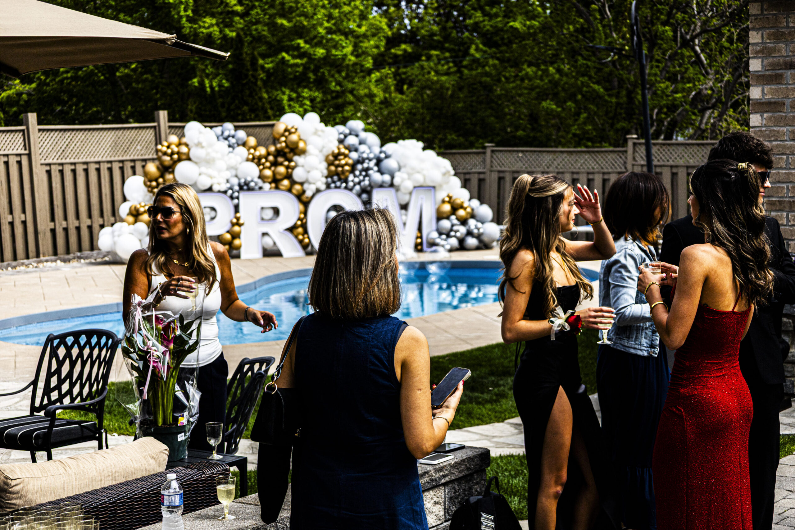 Guests mingling by a pool with PROM marquee letters and balloon garland