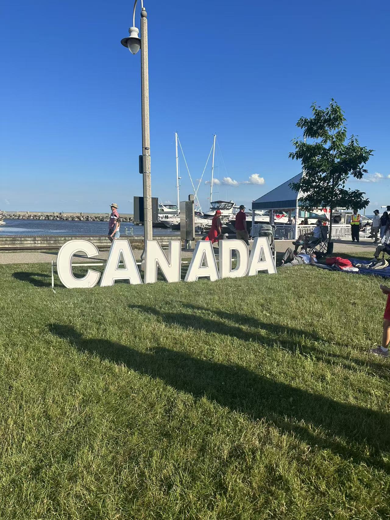 White marquee letters spelling CANADA on grass at a sunny marina