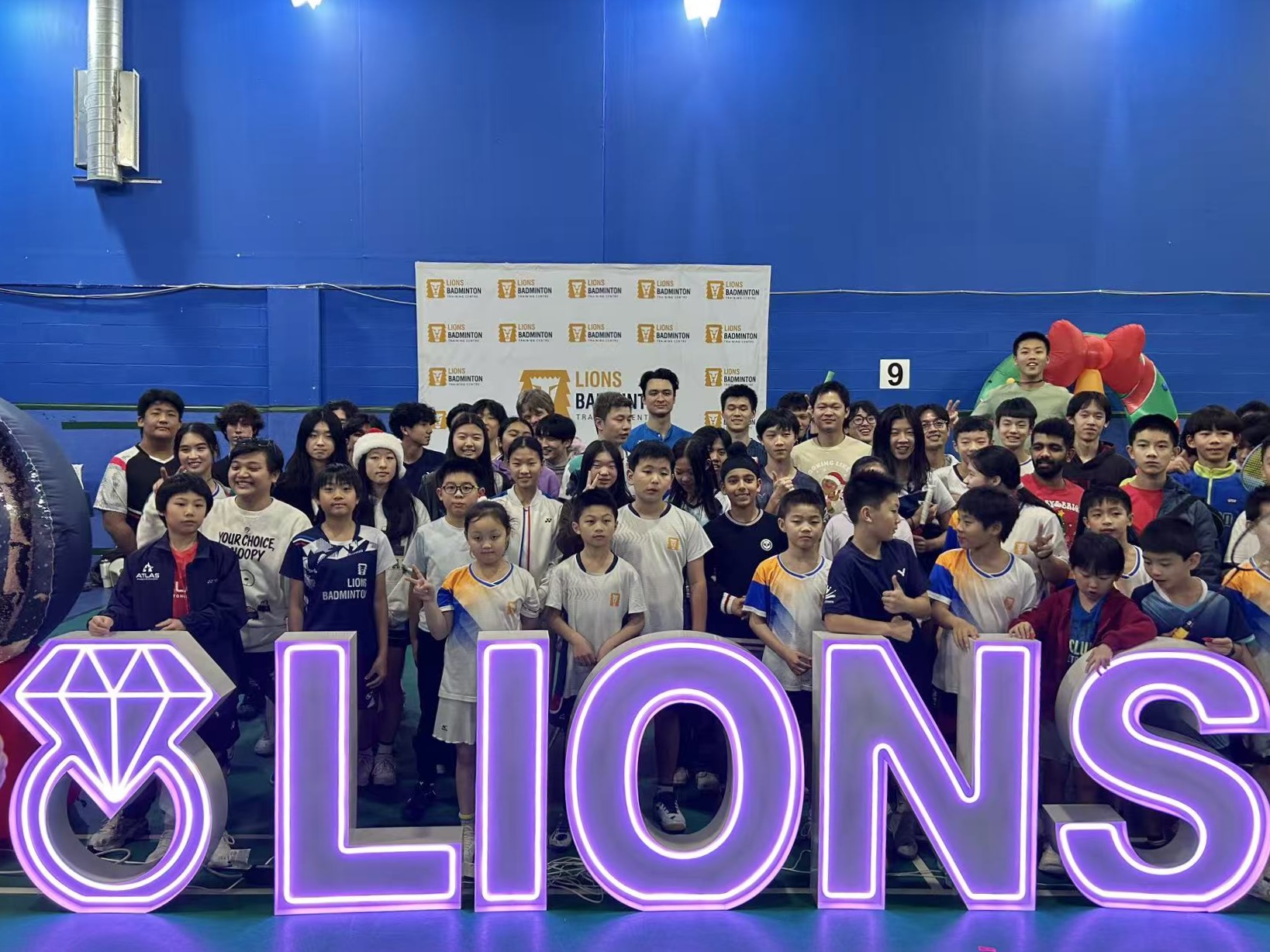 Purple neon letters spelling LIONS with children at a badminton event