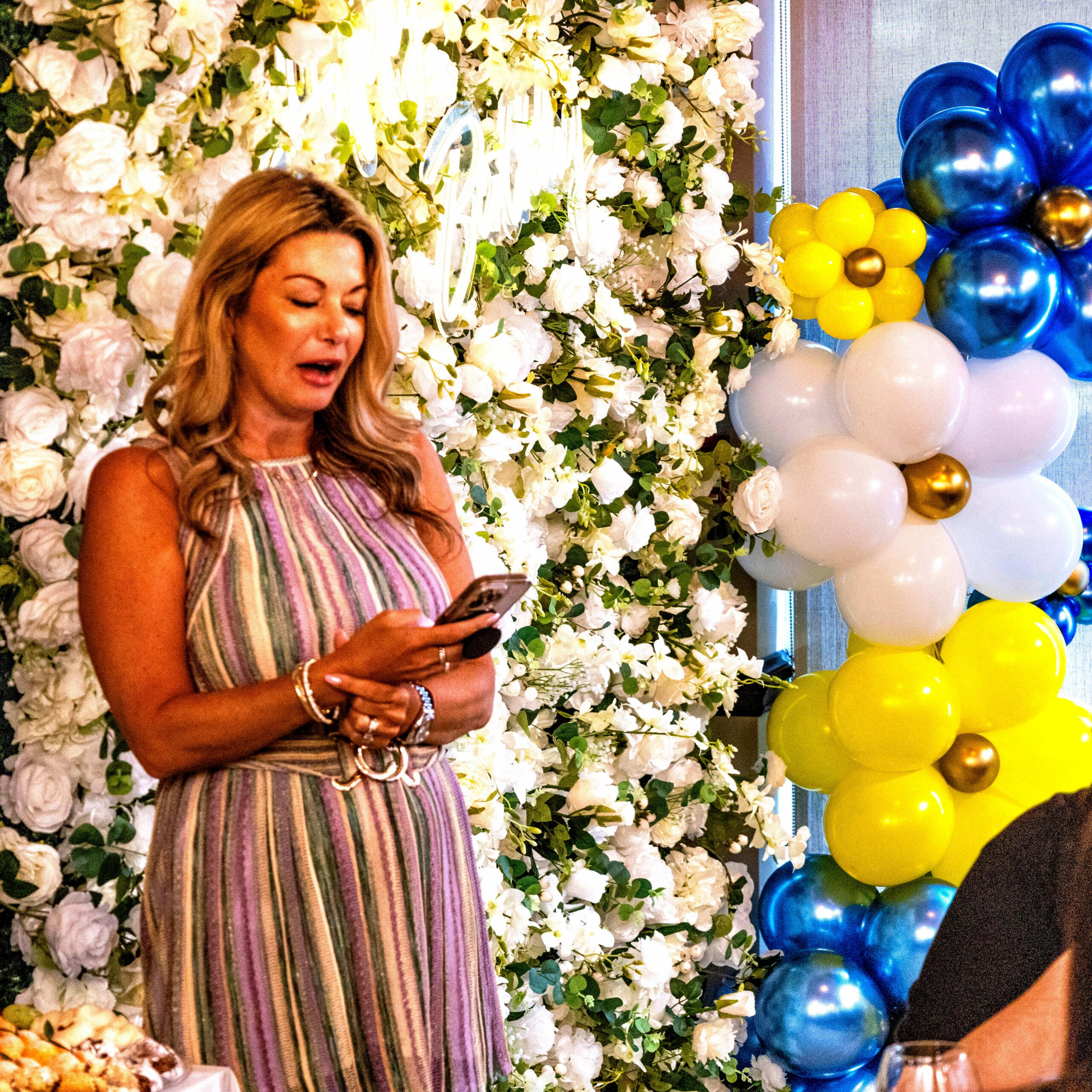 Woman giving a speech before a flower wall with a Celebrate neon sign