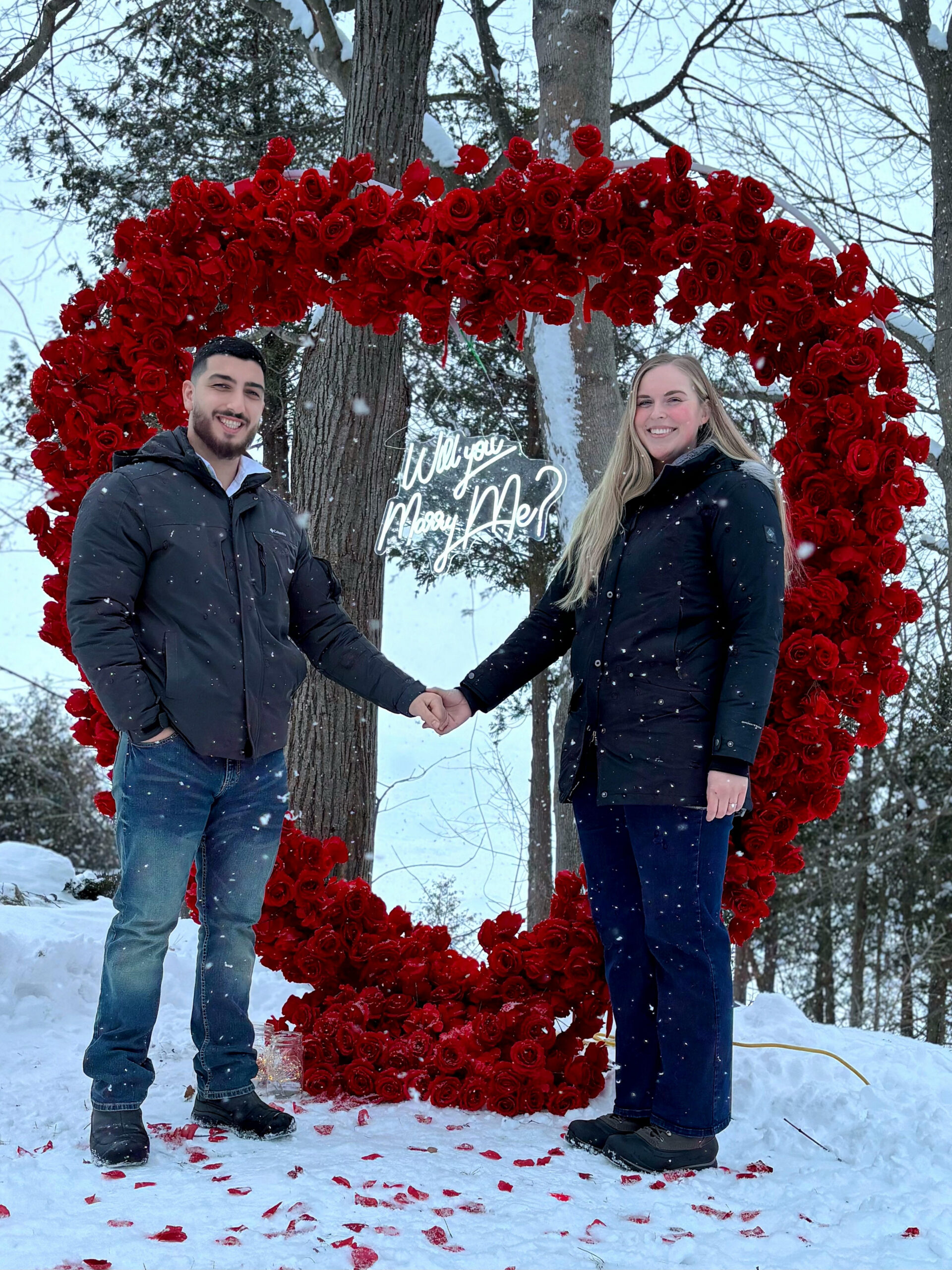 Couple holding hands before a giant heart of red roses in the snow